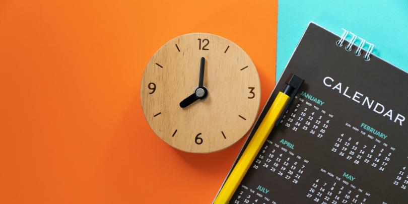 photo of wooden clock on orange and blue background next to black calendar