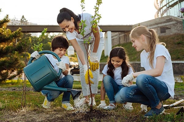 three kids and woman watering a plant outside