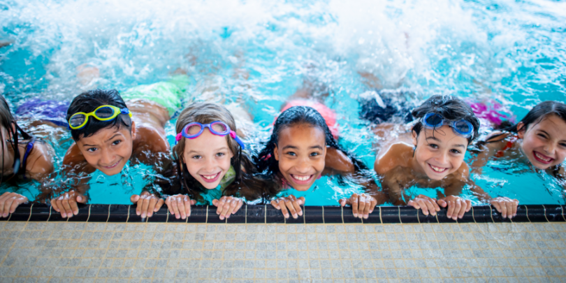 photo of kids swimming at the edge of the pool with their hands on the side looking up