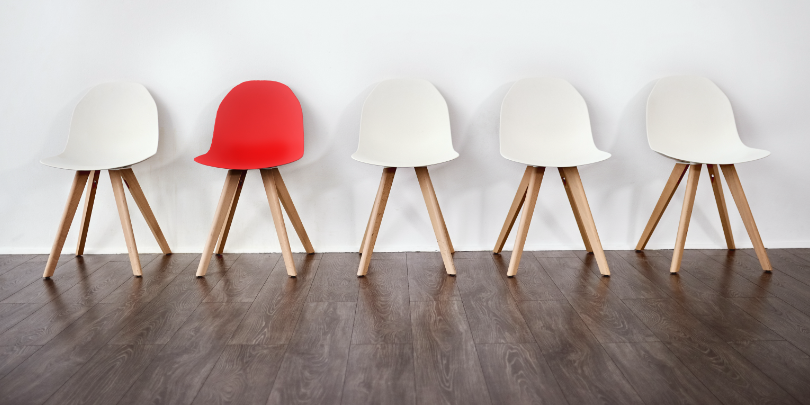 image of five chairs in front of a white wall, four are white and one is red