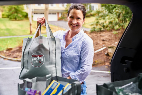 volunteer holding bag with grocery supplies in the back of a car