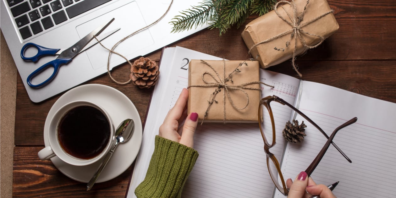 photo of desk with laptop coffee and two hands putting together gifts