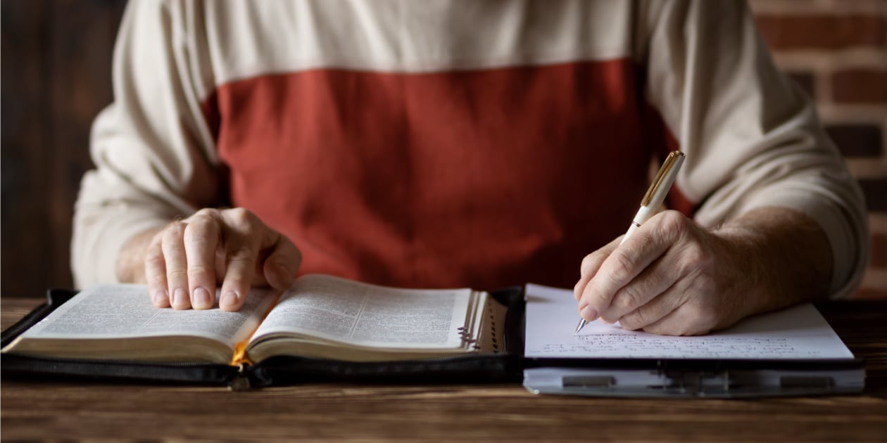 photo of person reading the bible and taking notes in a notebook