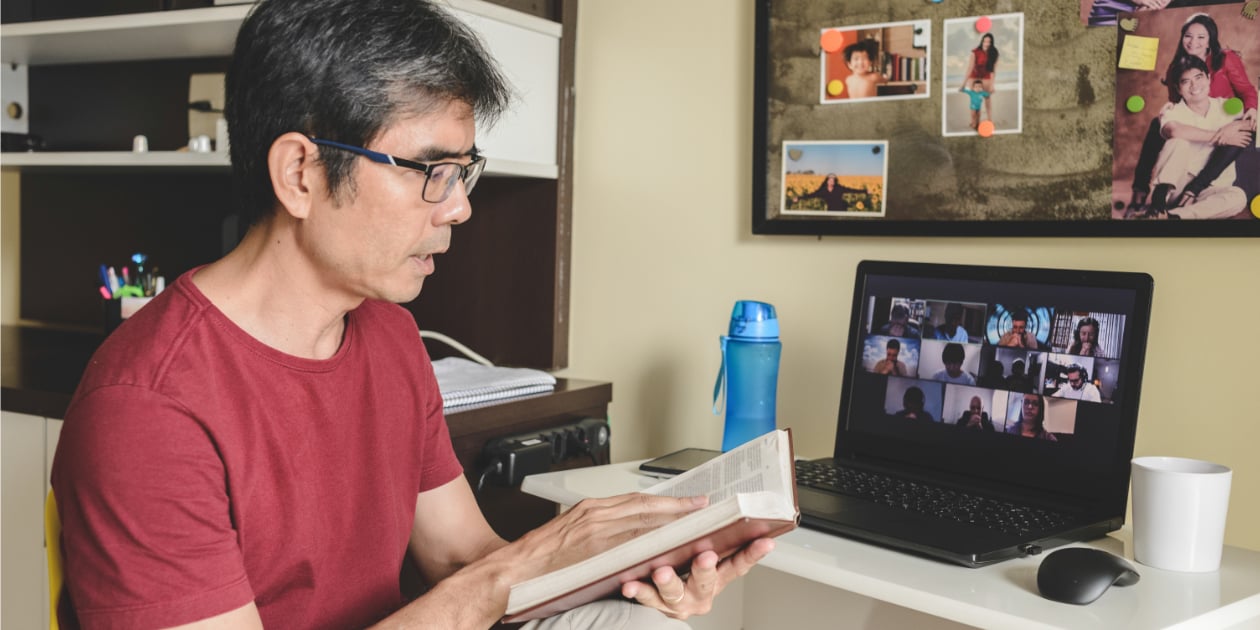 man holding a bible sitting in front of a computer with people on a video call