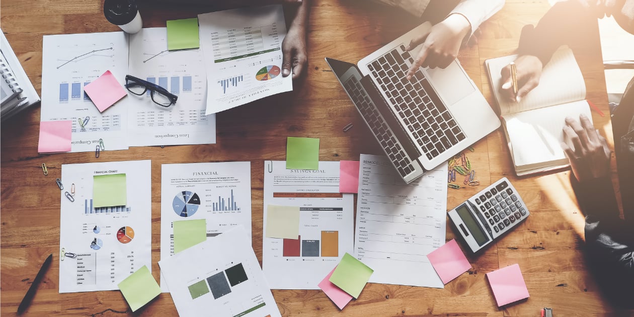 photo looking over a desk with pages of graphs, sticky notes, people working together