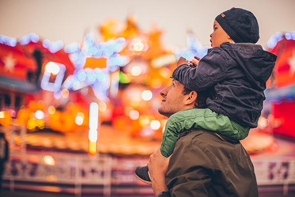 child on dad's shoulders walking at fall carnival