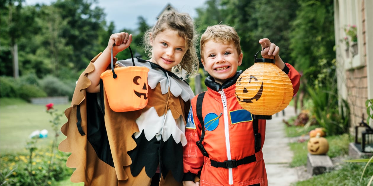 photo of a little girl and boy in eagle and astronaut halloween costumes holding pumpkin bins