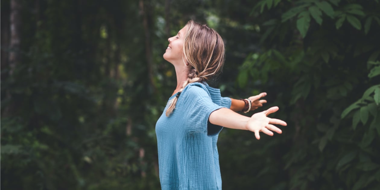 photo of women in the woods holding her arms open with a peaceful look on her face