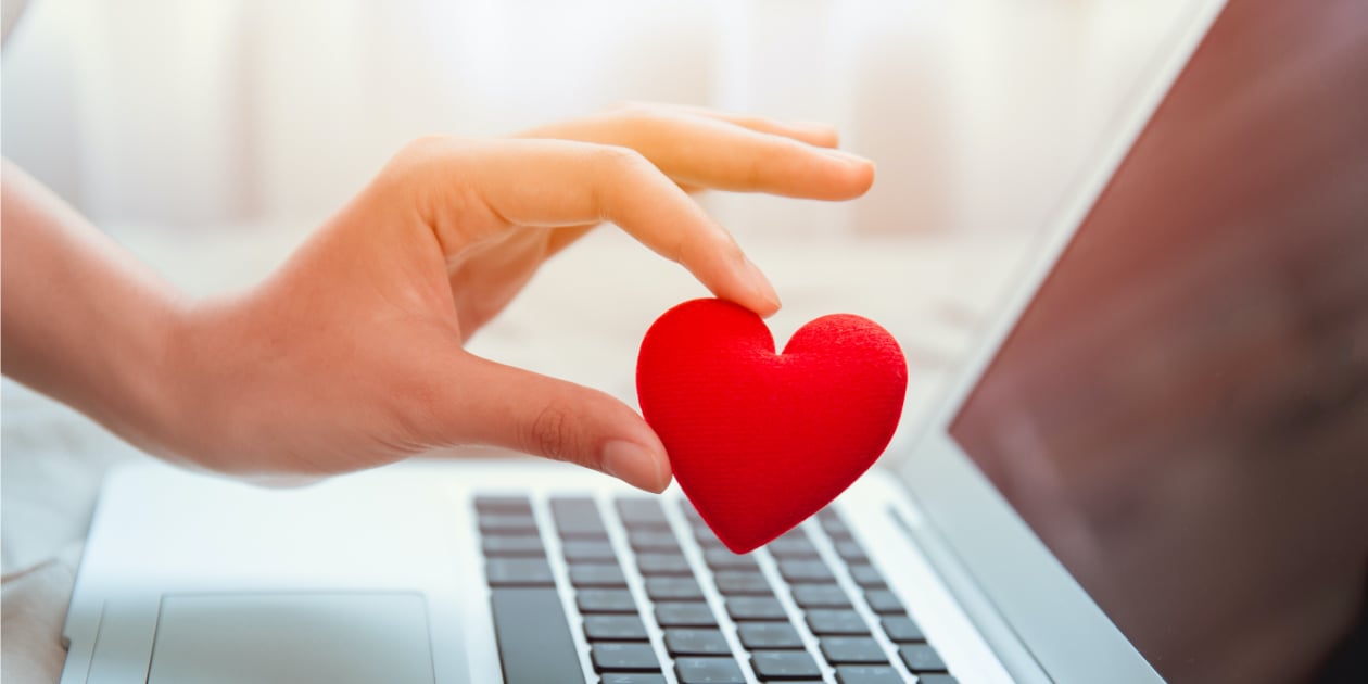 photo of person holding a red felt heart over a laptop computer