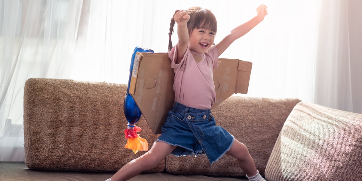 photo of little girl playing on a couch wearing a makeshift rocket