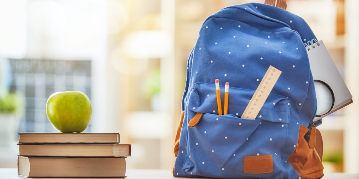 green apple on top of pile of books next to blue backpack